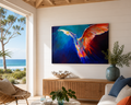Living room with a colorful abstract painting of a bird on the wall, large windows showing a beach view, and decorative items.
