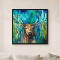 A framed square canvas print of an expressive painting featuring a brown deer with large antlers against a vibrant blue and green background, hanging on a beige wall above a light-colored sofa with neutral pillows.