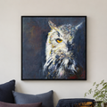 A framed square canvas painting of an owl's head in profile, displayed on a light beige wall above a sofa with dark blue and gray cushions. The painting features textured brushstrokes in white, gray, black, and subtle warm tones, with a yellow eye.