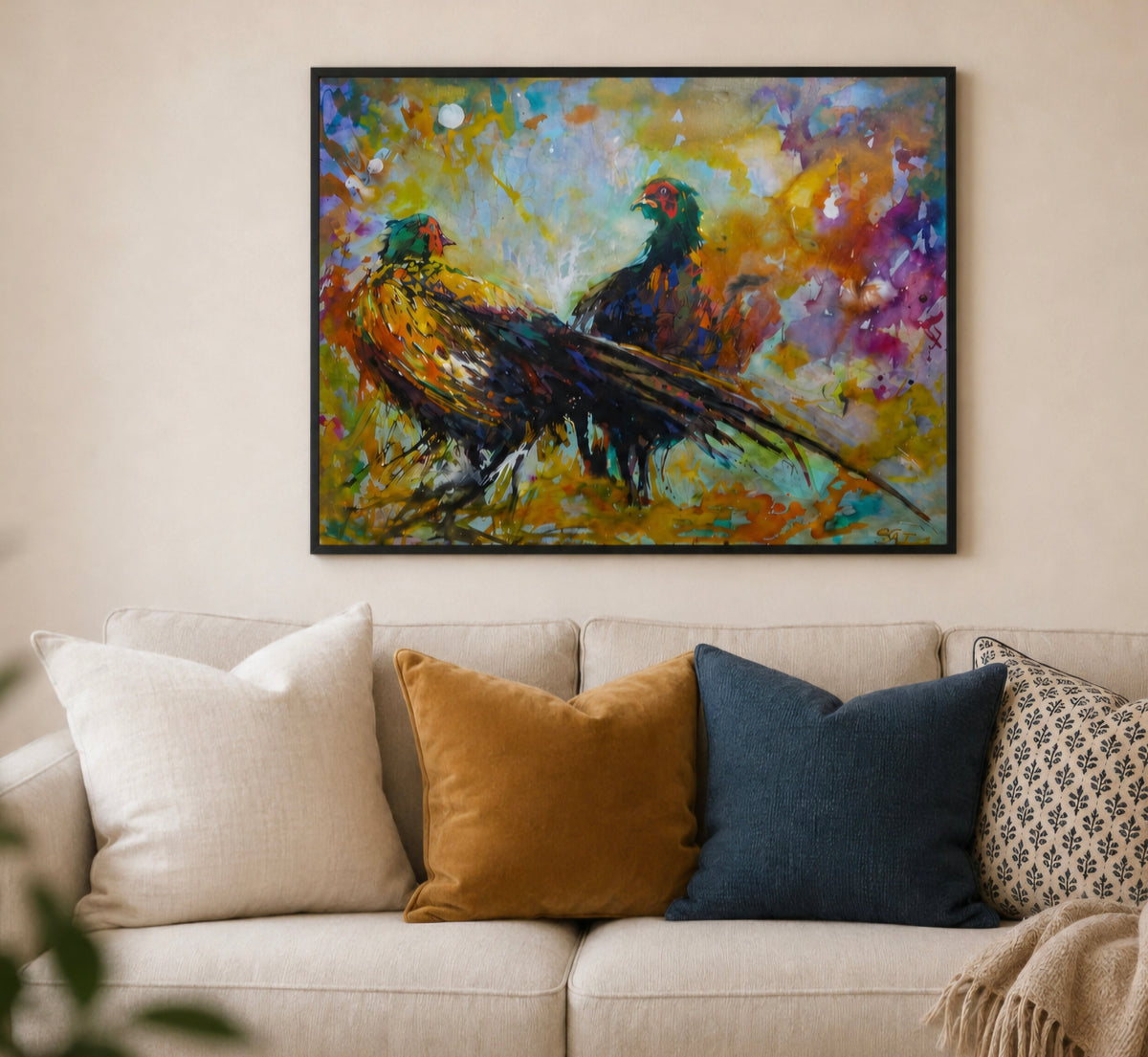 A framed colorful painting of two pheasants hanging on a beige wall above a light-colored sofa with decorative pillows.