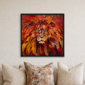 A framed square canvas print of a vibrant, textured lion painting in warm red, orange, and yellow tones, hanging on a light beige wall above a sofa with neutral-toned pillows.