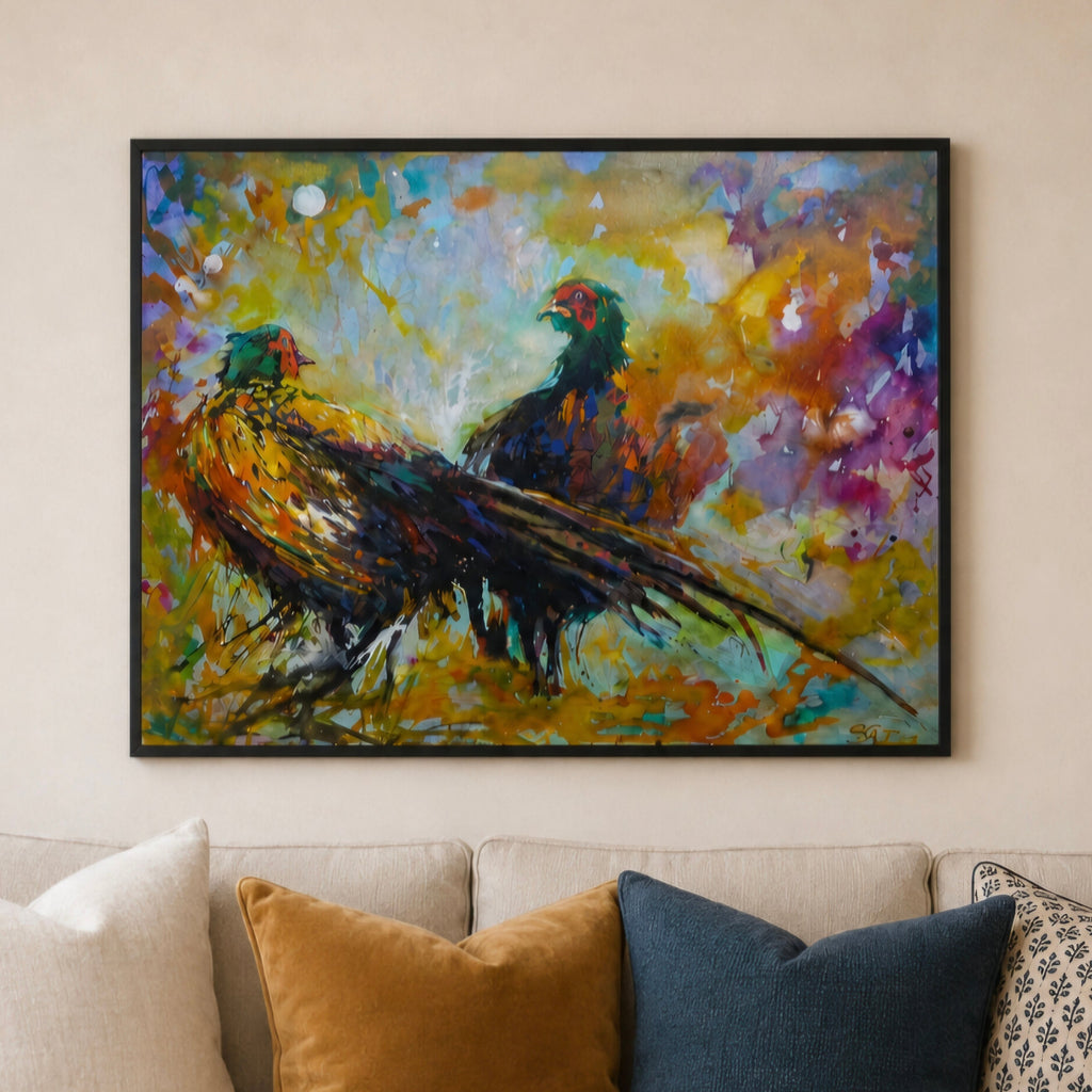A colorful framed painting of two pheasants hanging on a beige wall above a sofa with cream, mustard, navy, and patterned pillows.