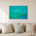 An abstract canvas painting with vibrant turquoise, teal, and green brushstrokes, displayed on a beige wall above a light beige sofa with decorative pillows.
