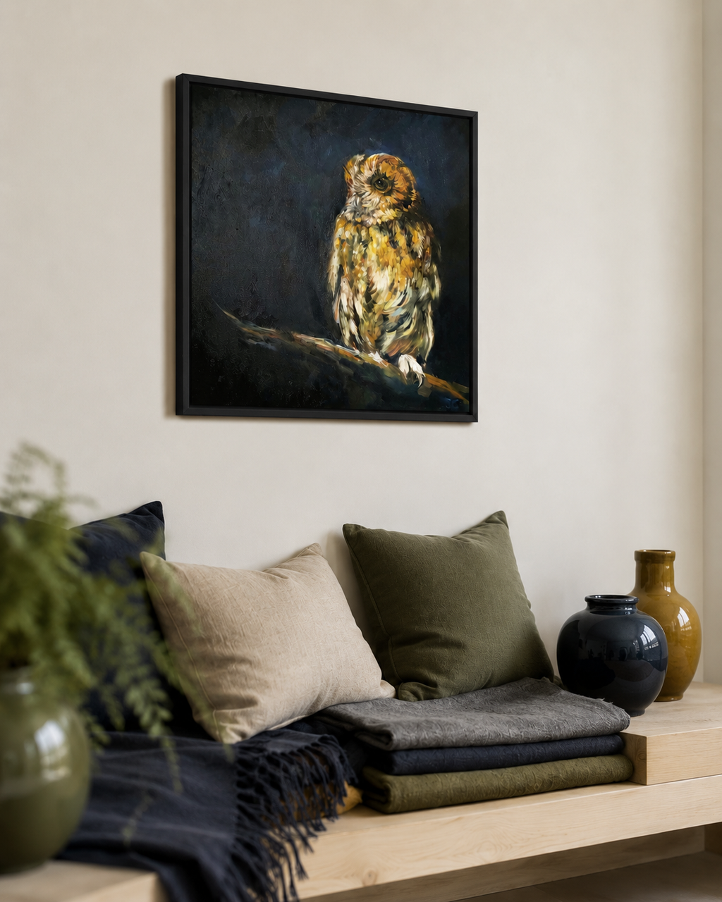 A framed square canvas painting of a brown and gold owl perched on a branch against a dark background, displayed on a beige wall above a styled wooden bench with pillows and vases.