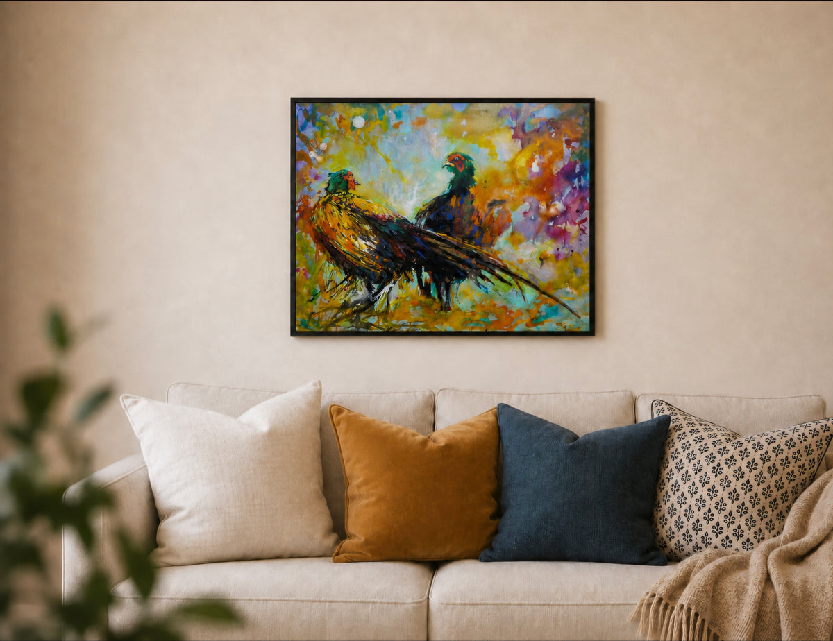 A framed colorful painting of two pheasants hanging on a beige wall above a light-colored sofa with decorative pillows.