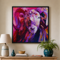 A colorful framed wall art print depicting a stylized ram head in vivid purple, pink, and red tones, displayed in a real home interior above a wooden console table.