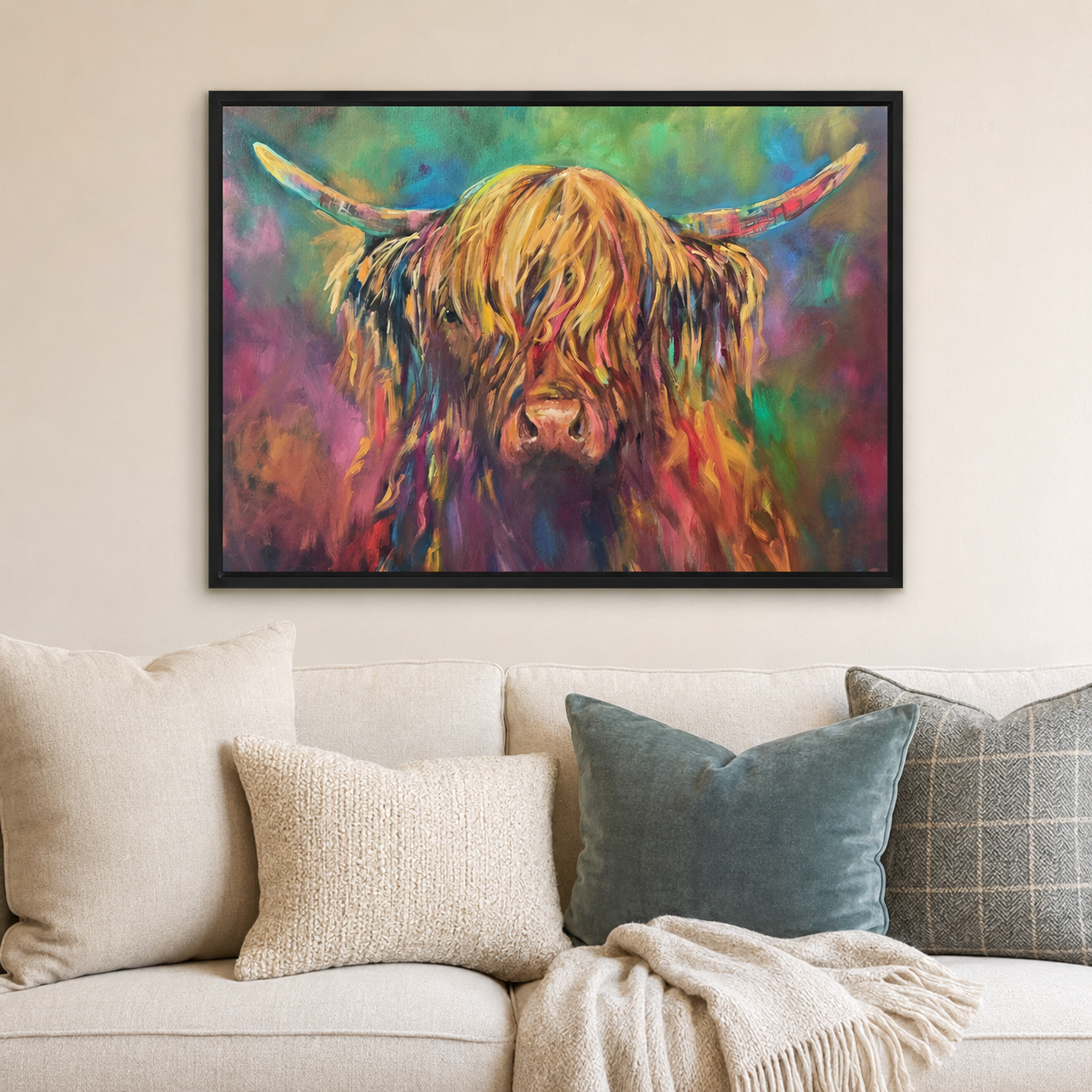 A framed colorful painting of a Highland cow hangs on a beige wall above a light-colored sofa with decorative pillows and a throw blanket.