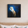 A square framed canvas painting of a barn owl in white and brown tones against a deep blue background, displayed on a beige wall above a wooden headboard with white pillows.
