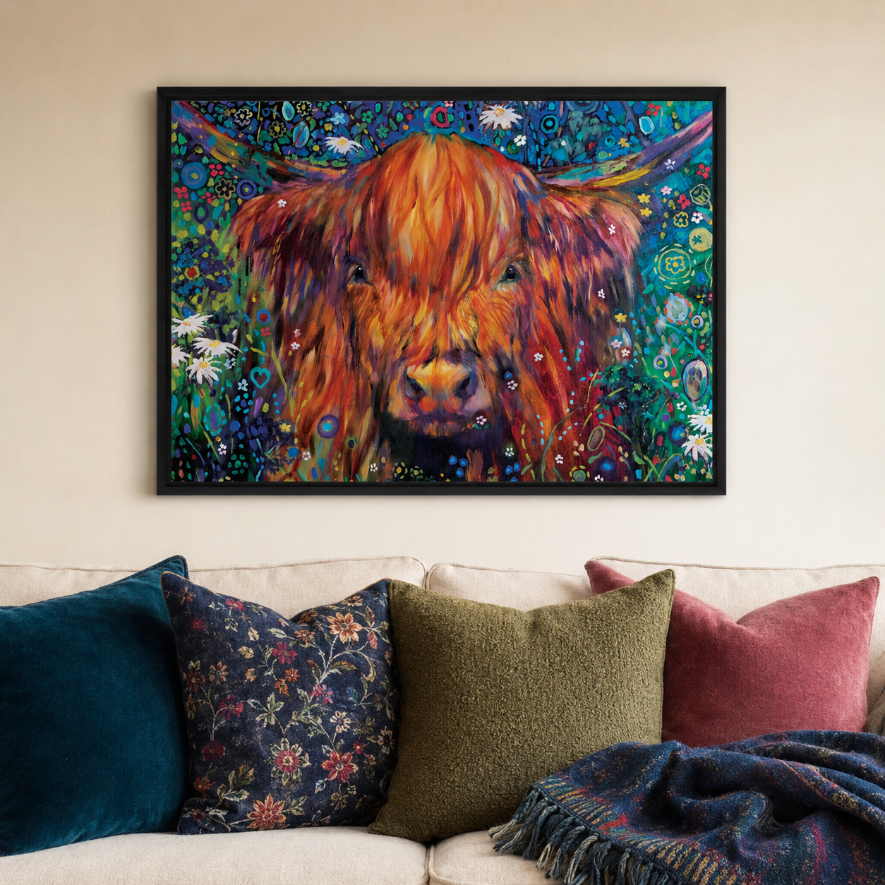 A framed colorful painting of a Highland cow hanging on a beige wall above a sofa with decorative pillows and a throw blanket.