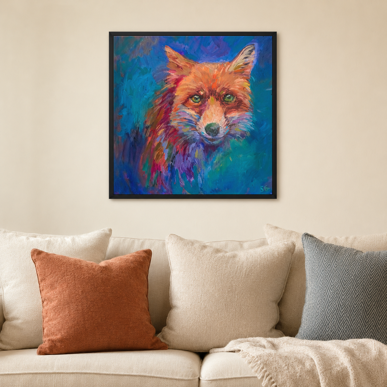 A colorful framed painting of a fox on a blue background, displayed on a beige wall above a sofa with cream and rust pillows.