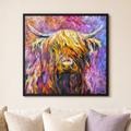 A framed square canvas print of an expressive, colorful Highland cow painting hanging on a beige wall above a sofa with neutral-toned pillows.