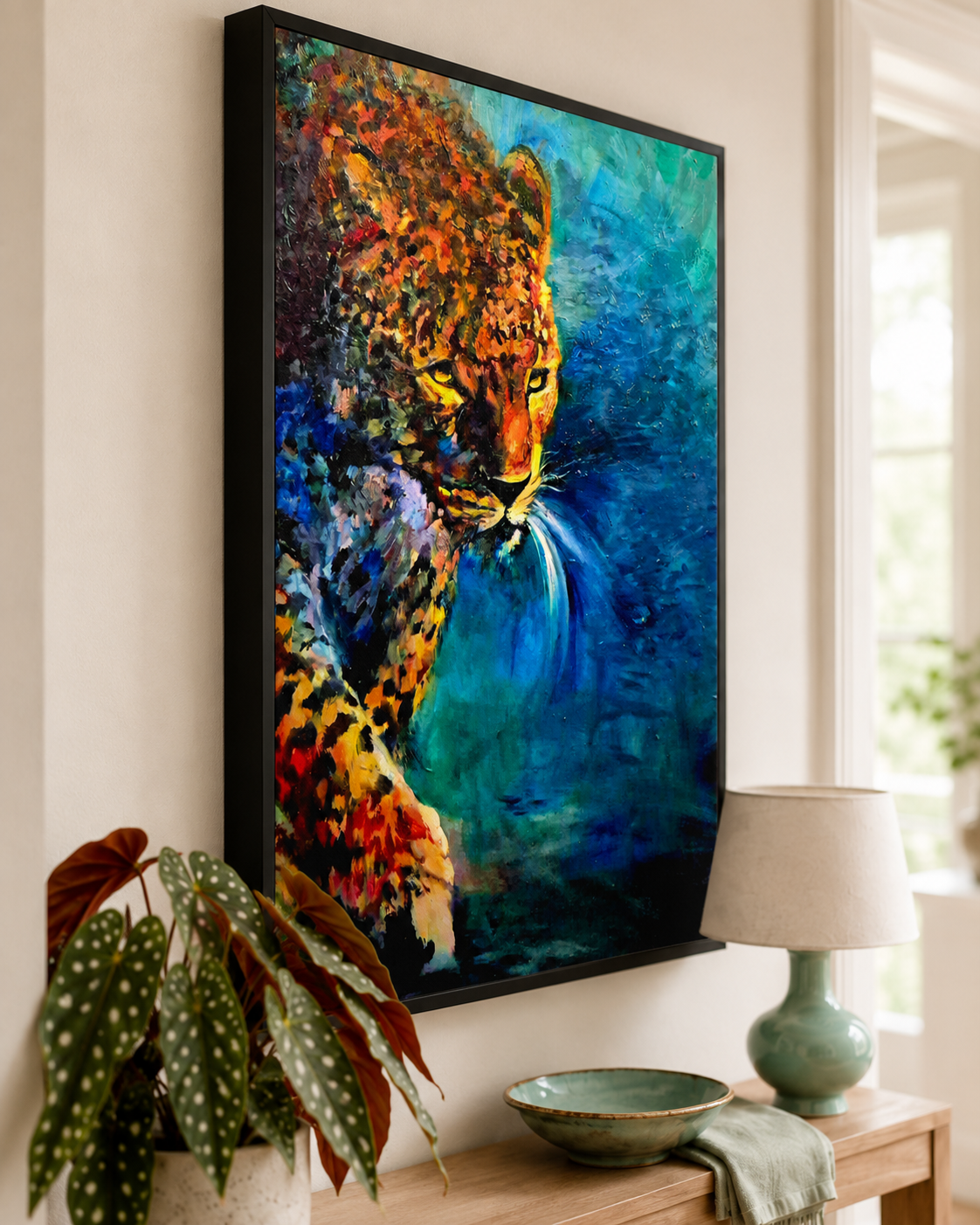 A framed vertical canvas art print depicting a colorful leopard in profile against a blue and teal background, displayed on a wall above a console table with a lamp, bowl, and potted plant.