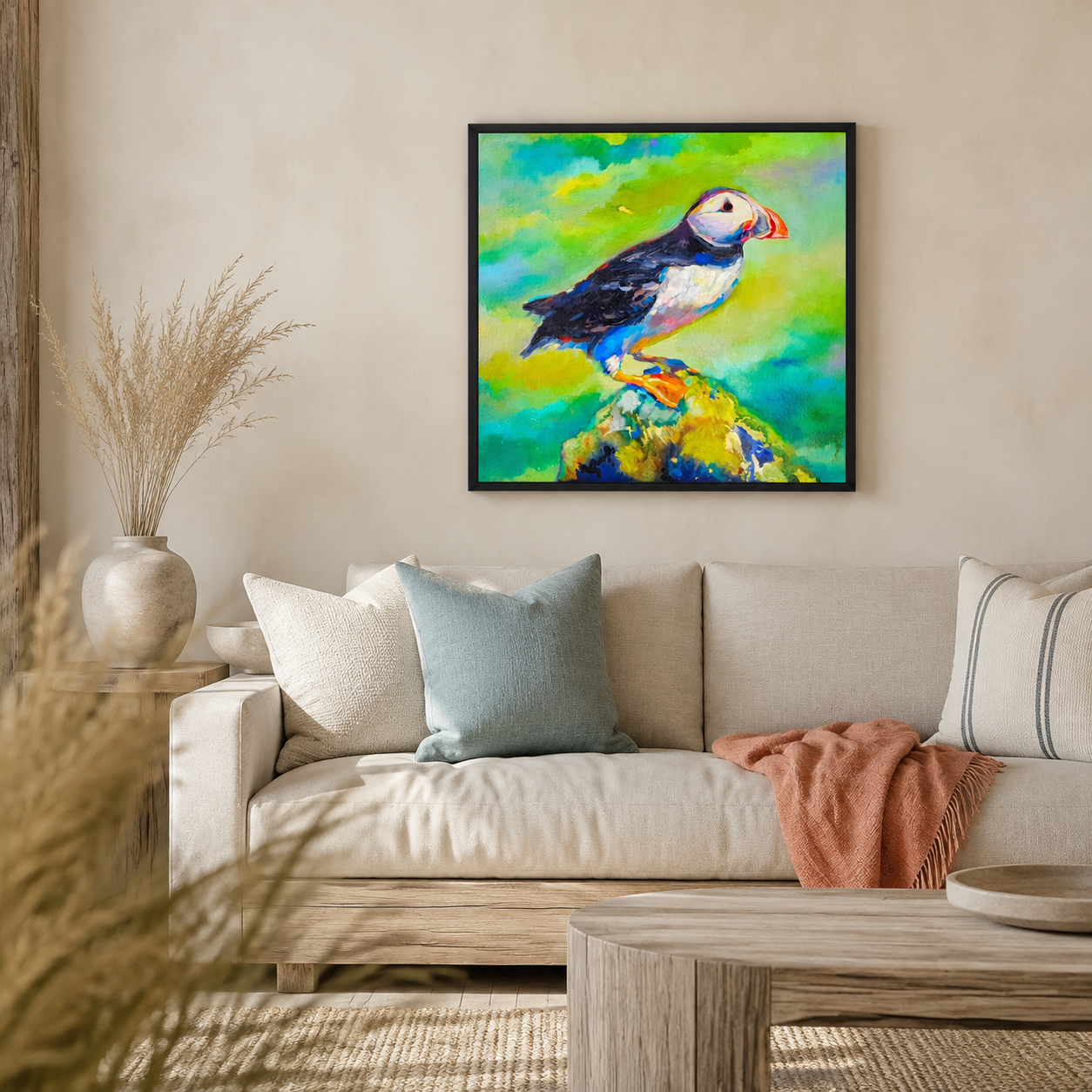 A framed colorful painting of a puffin hanging on a beige wall above a light-colored sofa in a styled living room.