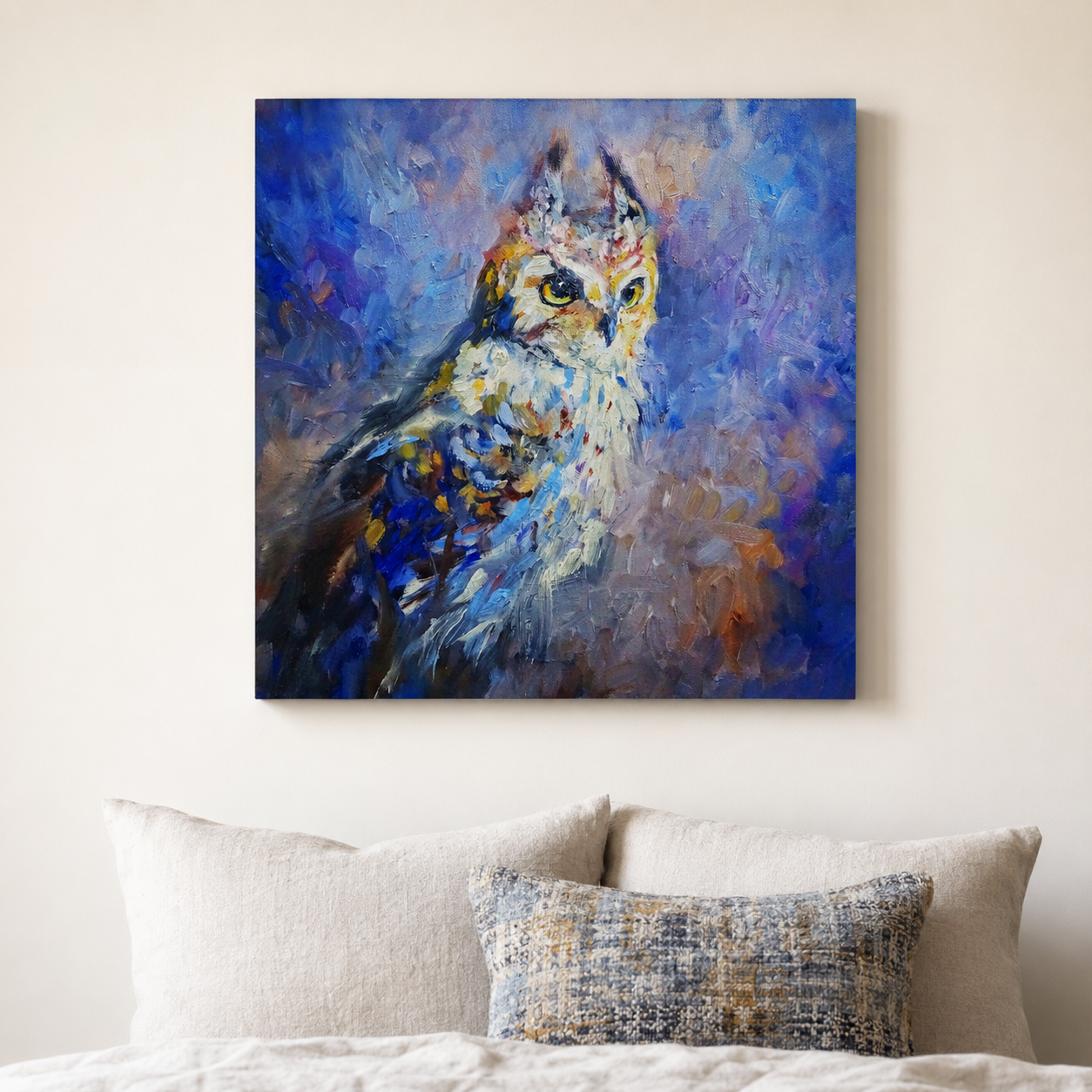 A square canvas wall art print featuring an impressionistic blue owl painting, displayed above a bed with neutral-colored pillows against a beige wall.