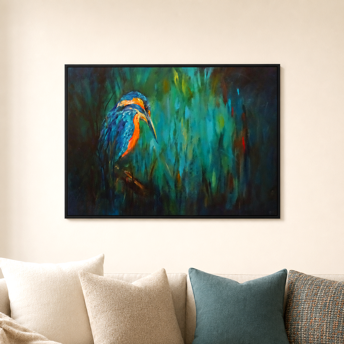 A framed horizontal canvas painting of a blue and orange kingfisher bird against a dark teal and green background, displayed on a beige wall above a sofa with neutral-colored pillows.