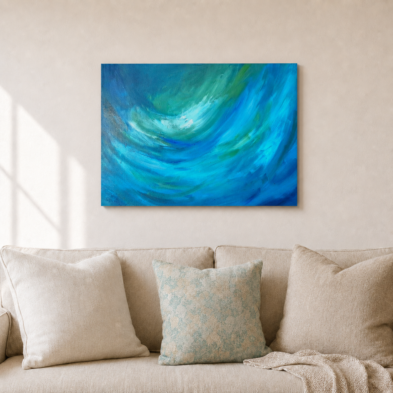 An abstract canvas wall art print featuring vibrant swirls of blue and green, displayed on a beige wall above a modern beige sofa with decorative pillows.